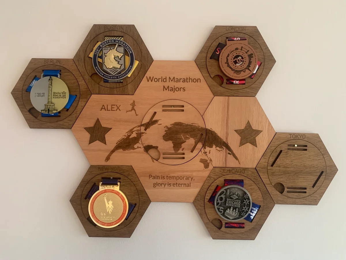 Pannello di legno a esagoni con le medaglie di Berlino, Boston, Londra, New York e Chicago e lo spazio ancora vuoto per Tokyo
