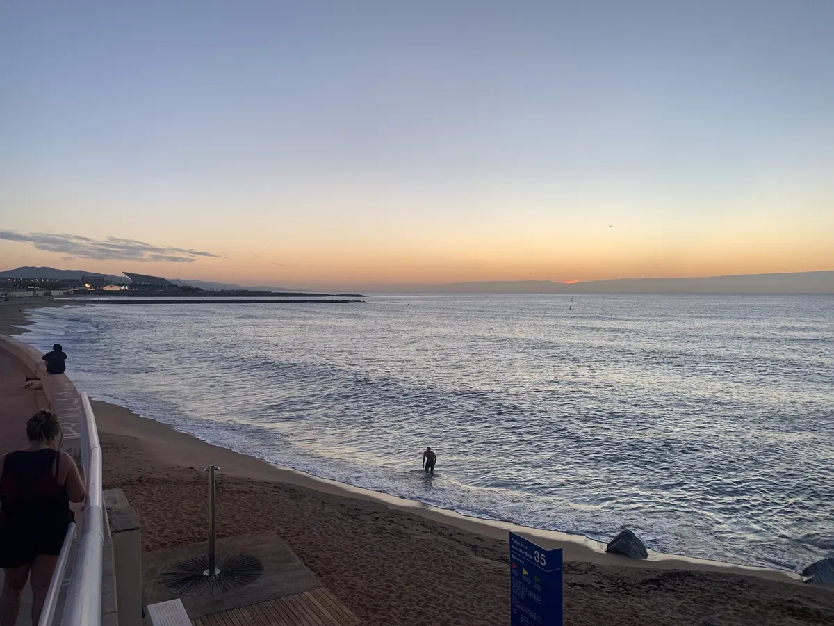 Spiaggia all'alba con una persona in acqua e il molo