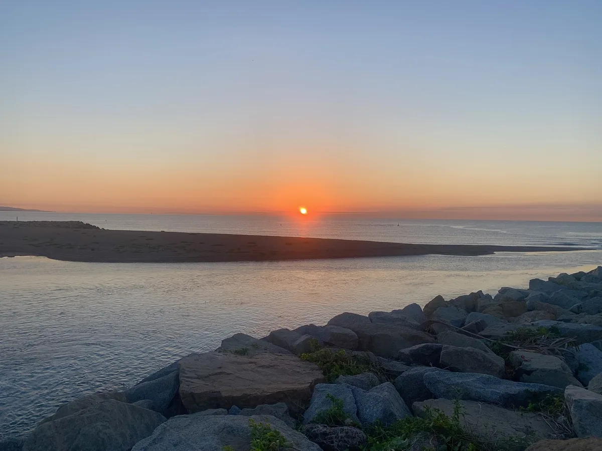 Sole che sorge sul mare dietro la scogliera di massi