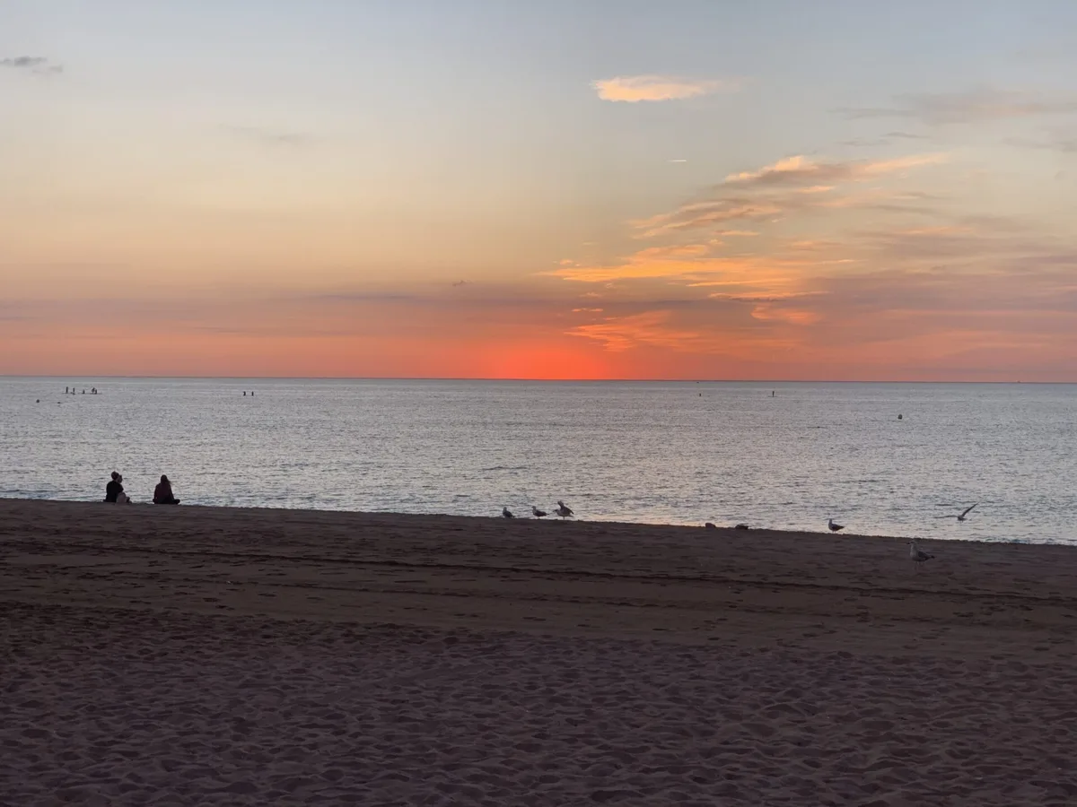 Sole rosso all'alba sul mare con due persone sedute sulla spiaggia