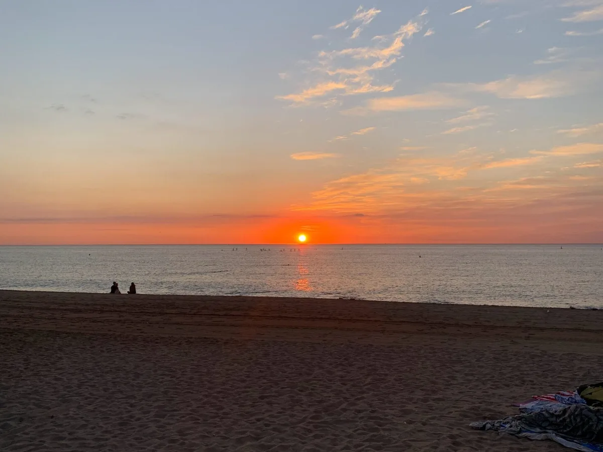 Sole che sorge sul mare con due persone sedute sulla spiaggia