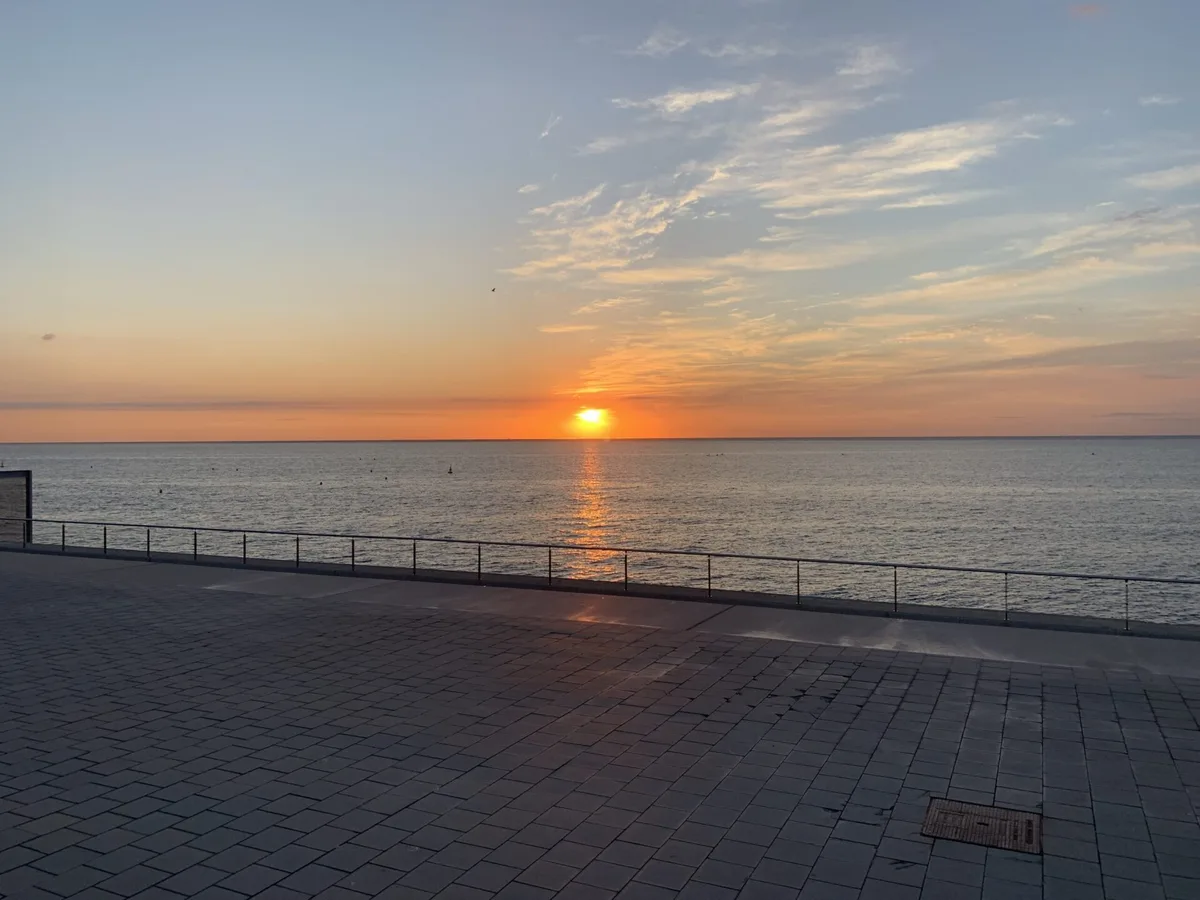 Sole che sorge sul mare dal lungomare con la ringhiera