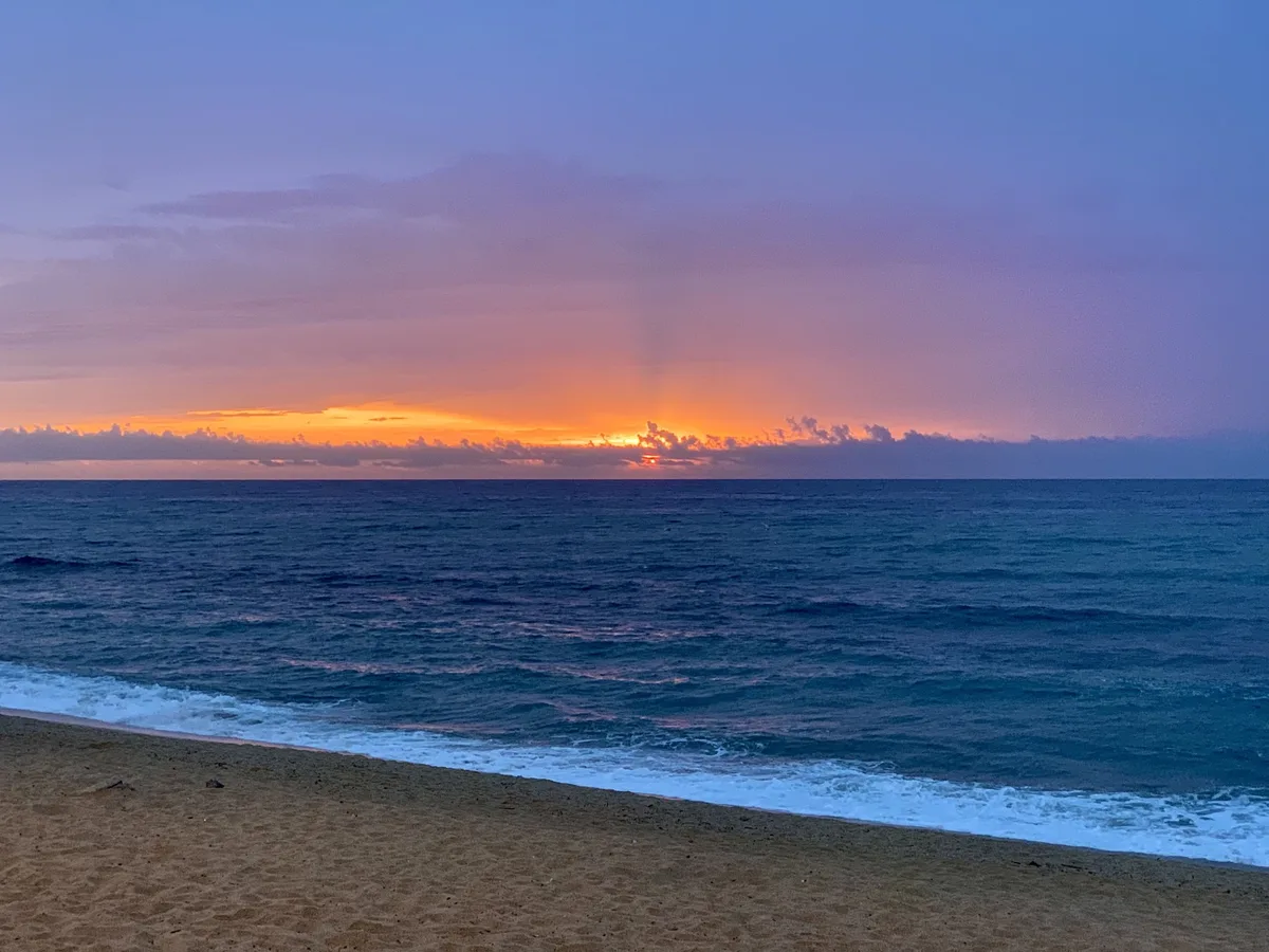 Alba arancione sul mare mosso con la spiaggia in primo piano