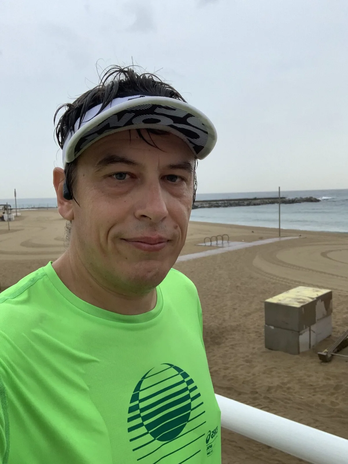 Selfie con visiera e maglia verde fluo sul lungomare con la spiaggia alle spalle