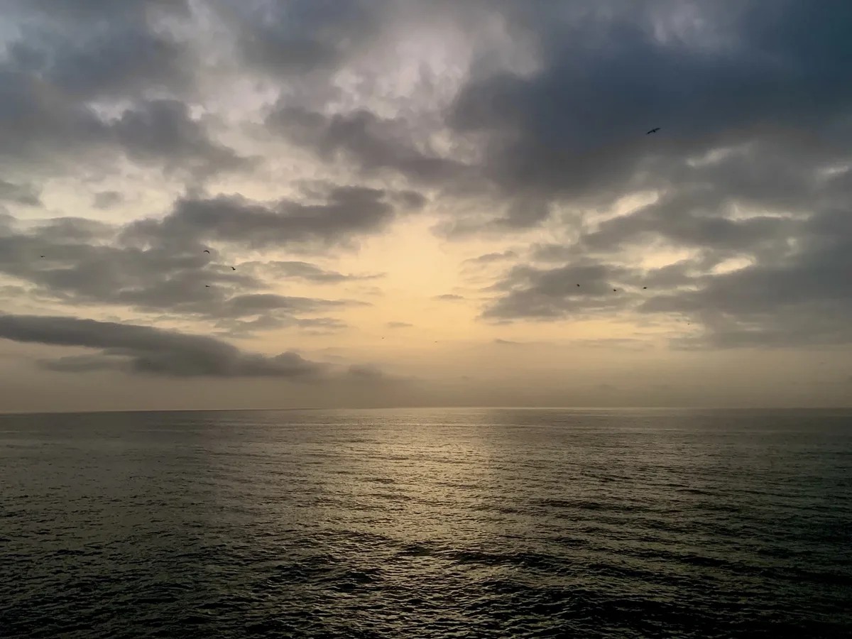 Cielo di nuvole scure e sole basso sul mare