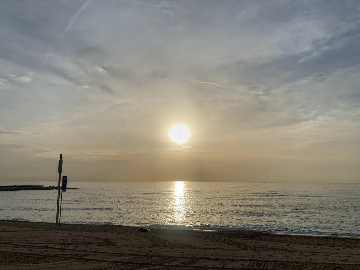 Sole velato sul mare con un palo sulla riva