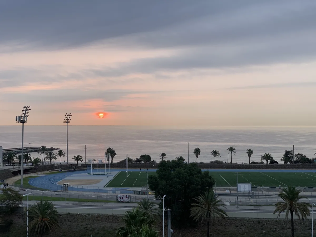 Sole rosso all'alba sopra un campo sportivo con le palme e il mare