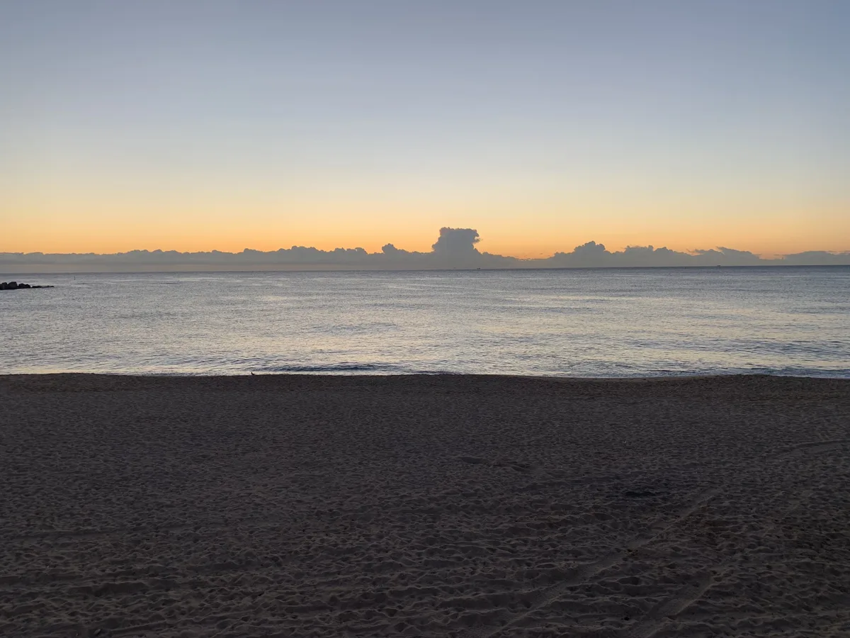 Spiaggia scura con nuvole sul mare all'orizzonte