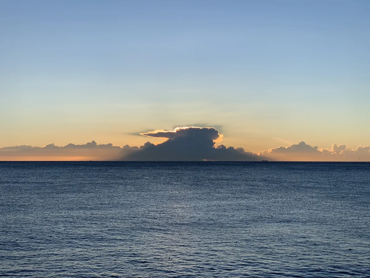 Mare calmo al tramonto con una nuvola scura all'orizzonte