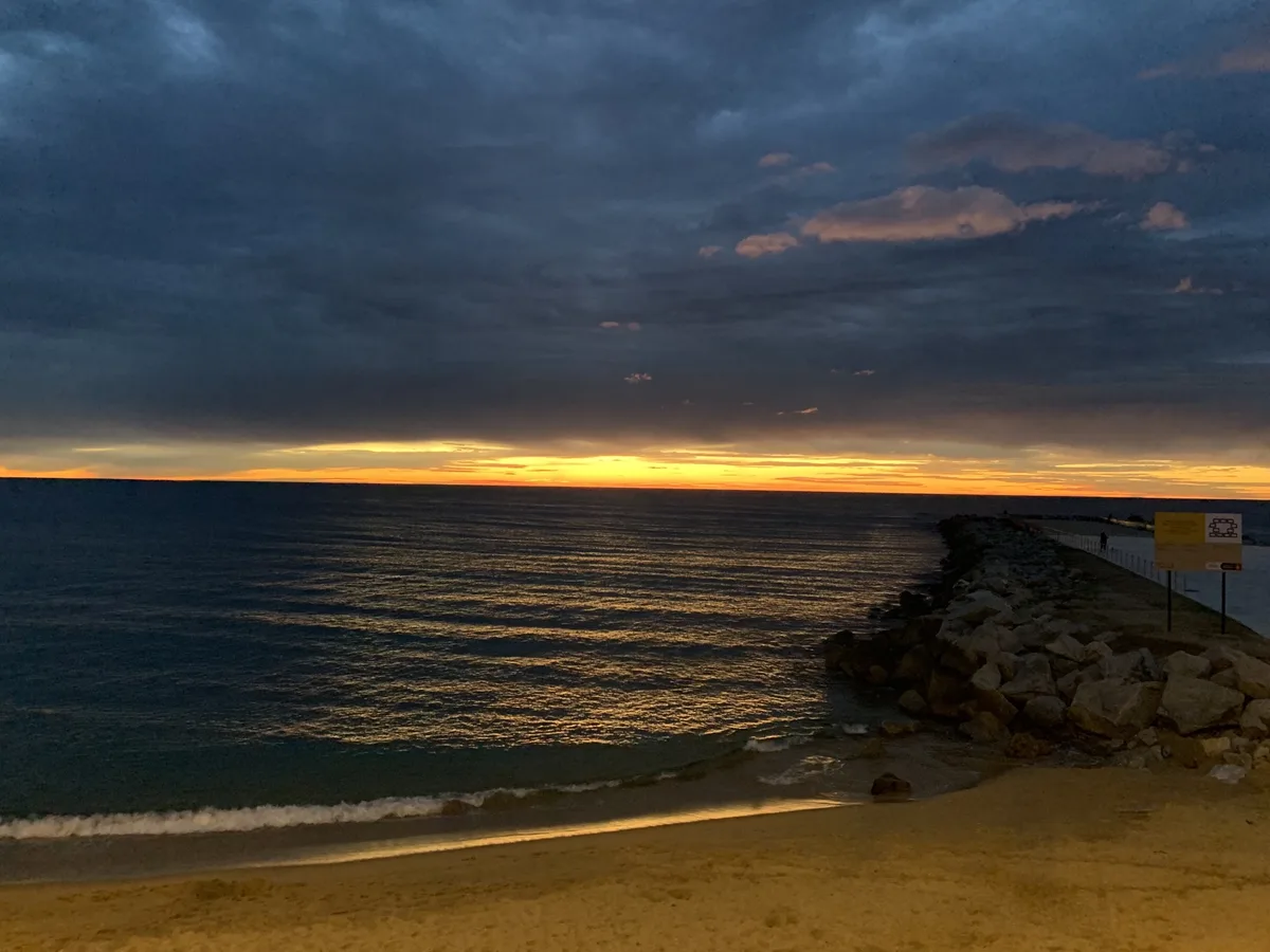 Tramonto arancione sotto nuvole scure con la spiaggia e un molo di massi