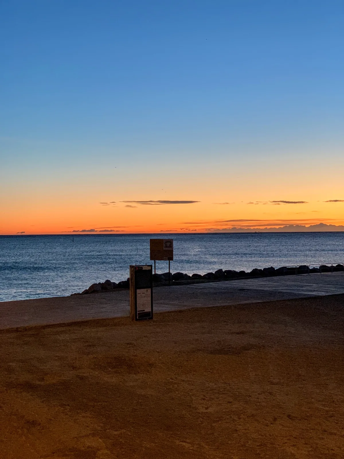 Tramonto arancione sul mare con un cartello sulla spiaggia