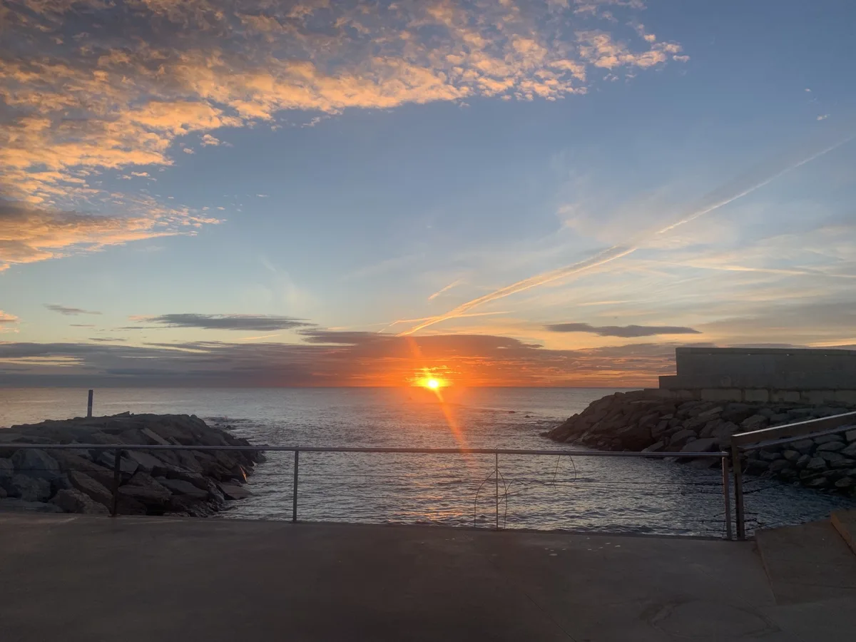 Sole che sorge dietro il molo di massi con raggi di luce