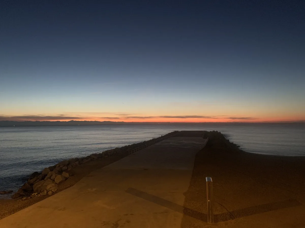 Molo di massi al crepuscolo con il cielo arancione sul mare