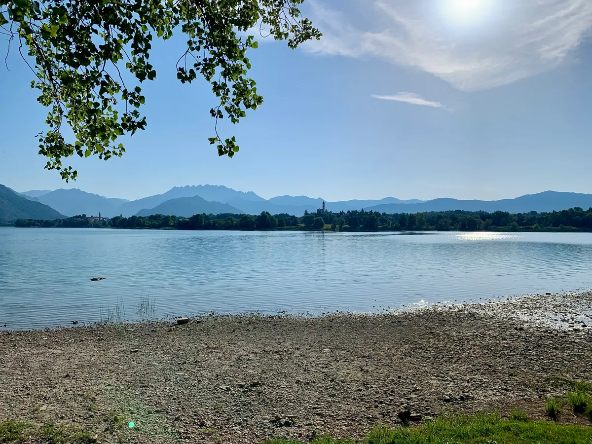 Lago calmo con le montagne sullo sfondo e la riva di ciottoli