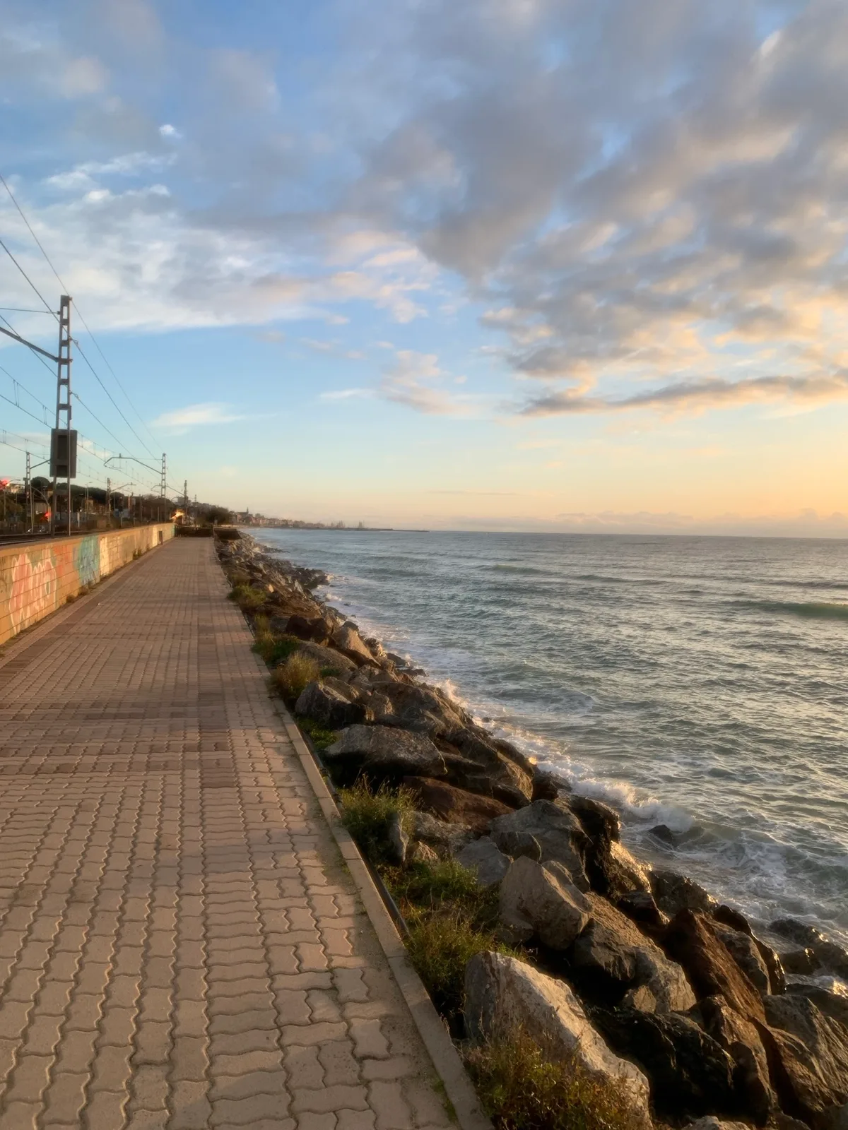 Marciapiede lungo la scogliera con la ferrovia e il mare all'alba