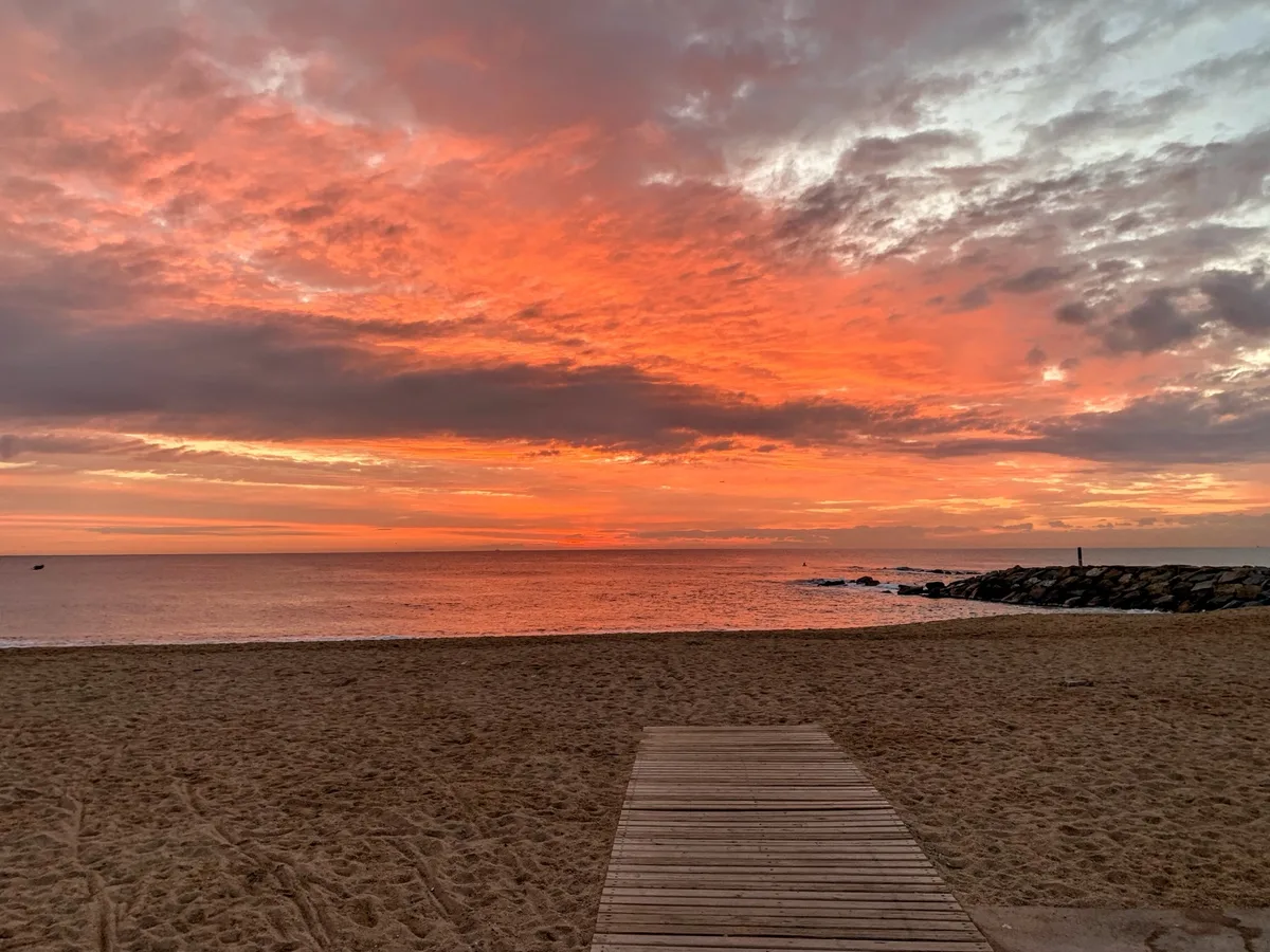 Alba rossa sul mare con una passerella di legno sulla sabbia