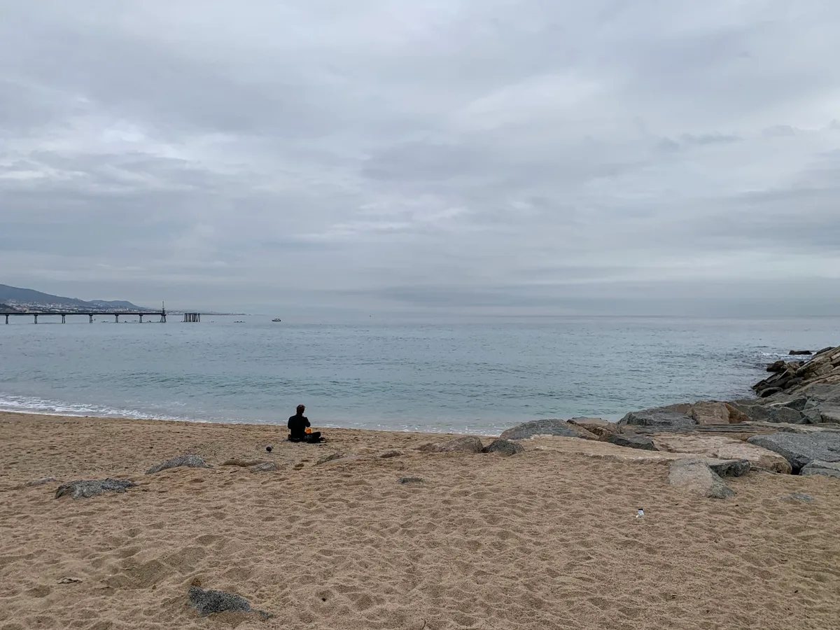 Spiaggia in inverno con il mare calmo e una persona seduta