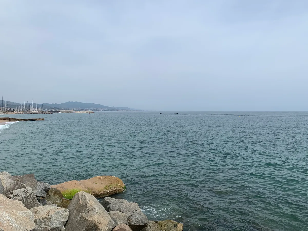 Costa di Barcellona con scogli e mare calmo sotto un cielo velato