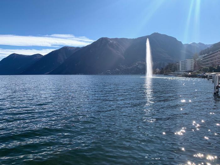 Getto d'acqua di una fontana sul lago con le montagne sullo sfondo