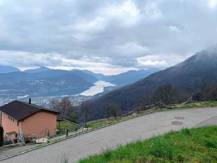 Strada in salita con una casa e il lago in lontananza
