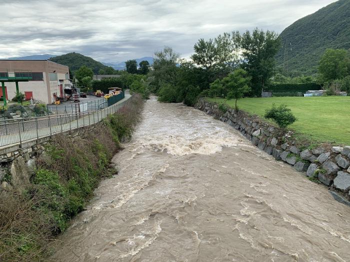 Torrente in piena con l'acqua marrone lungo la strada