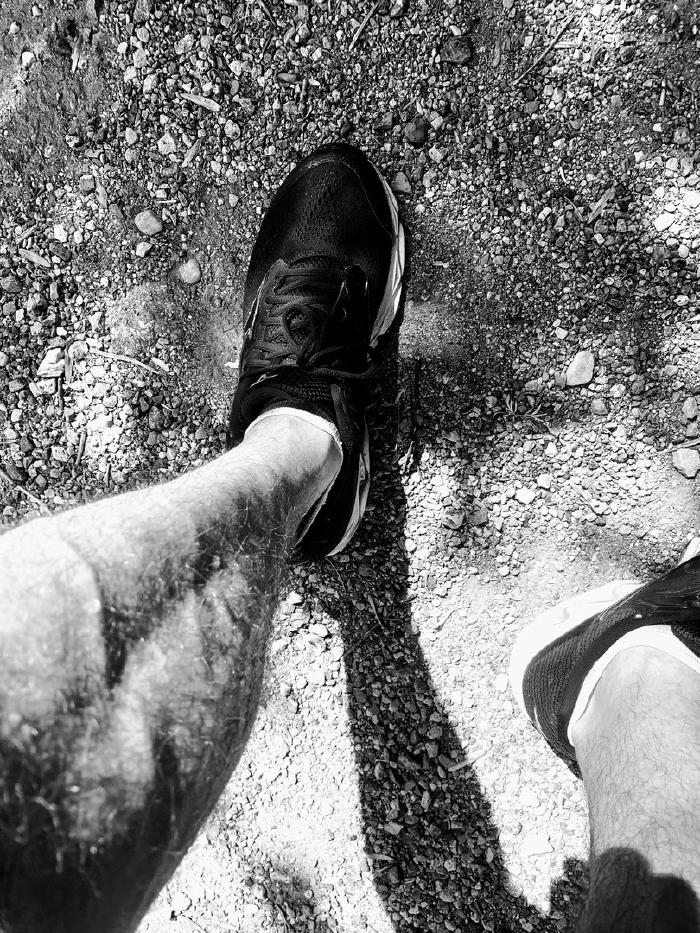Scarpa da corsa e gamba vista dall'alto sull'asfalto, in bianco e nero