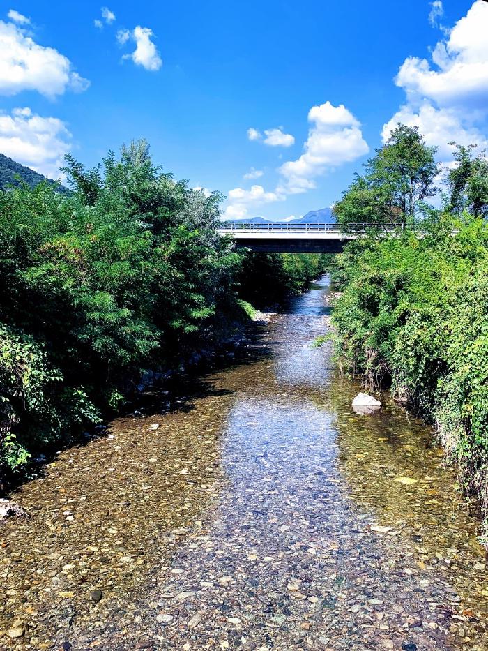 Torrente con acqua bassa e un ponte sotto un cielo azzurro