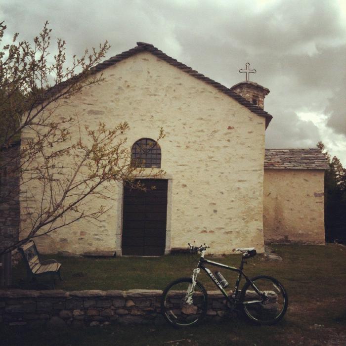 Piccola chiesa in pietra con una mountain bike appoggiata davanti